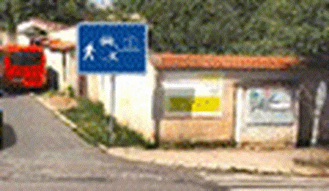 Zvětšený detail modré obdélníkové značky s domem, autem a hrajícím si dítětem nad ulicí naproti