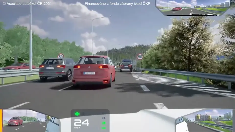 Pohled z kabiny auta na dvouproudou silnici, před kterou stojí a pomalu popojíždí kolona aut, rychlost 24 km/h
